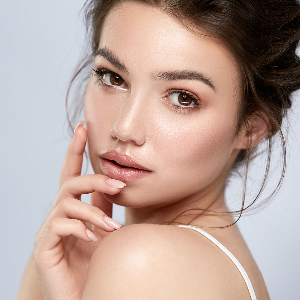 Young woman with smooth, full lips touching her face after natural-looking lip fillers in Little Rock